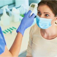 A healthcare worker takes the temperature of a female patient wearing a mask